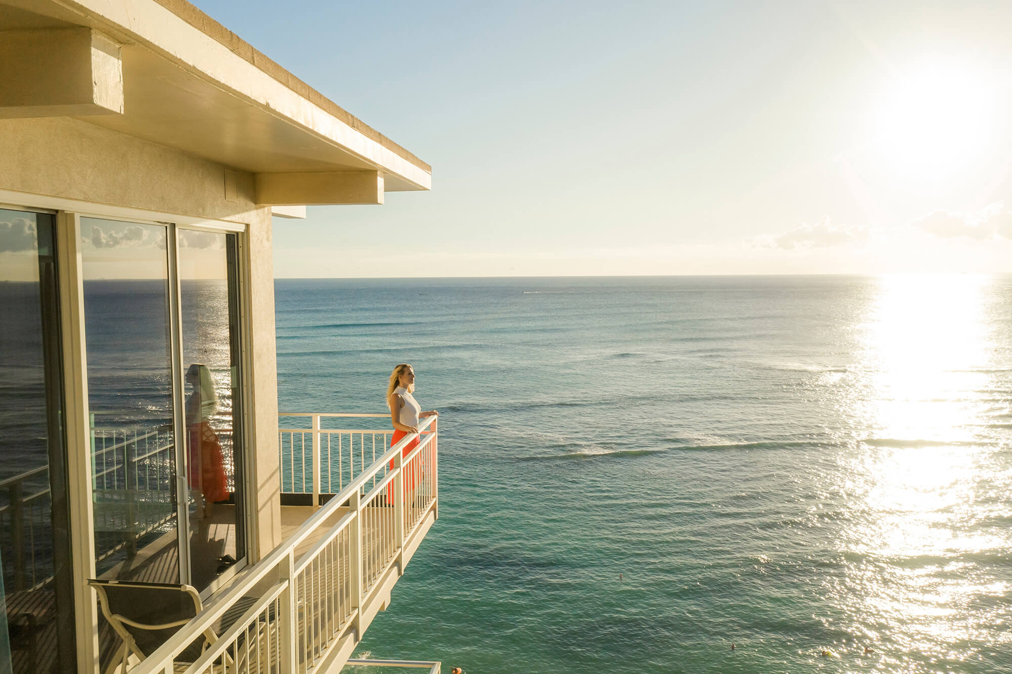 Guest at Kaimana room balcony, looking at Waikiki Beach ocean during sunset.